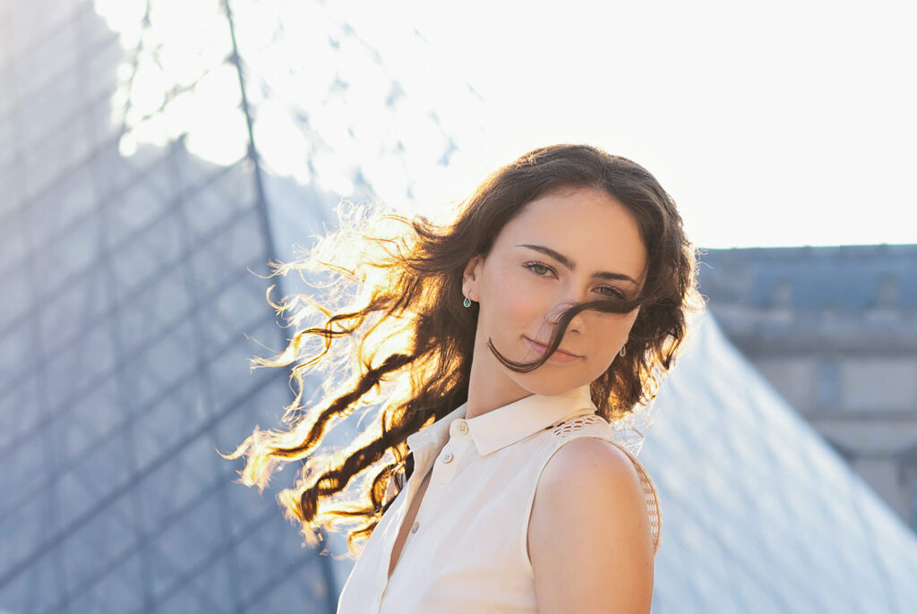 Editorial portrait photography of a girl smiling in front of the Louvre with the sun in her hair