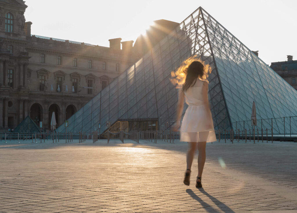 A girl in a white dress dancing in front of Louvre in the morning sun