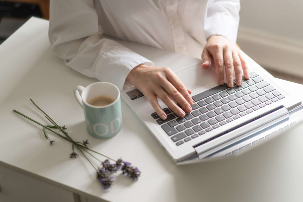 Woman's hands placed on a laptop keyboard with a coffee cup and some levander