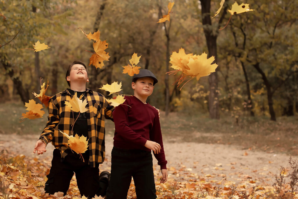 a family portrait of two brothers playing in Autumn leaves